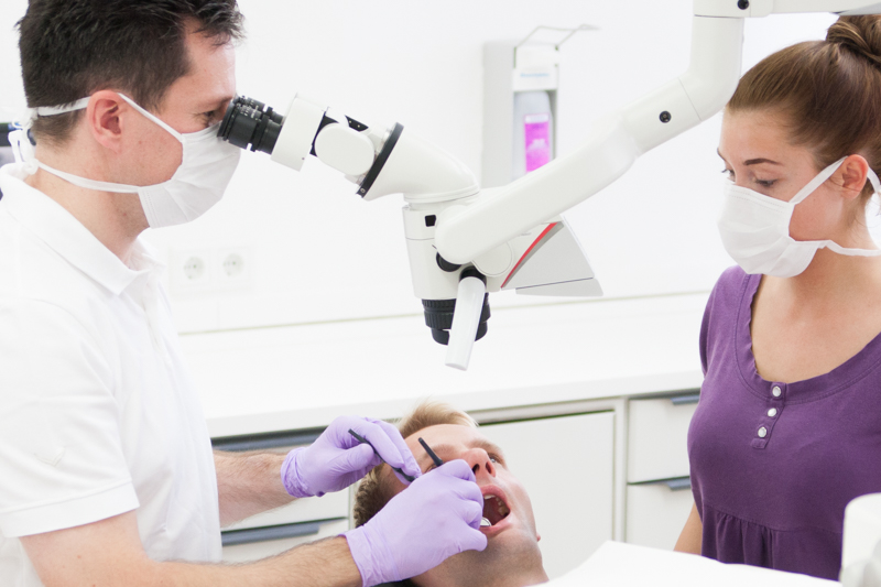 Dr. Frank Pawlak untersucht einen Patienten unter dem OP-Mikroskop, unterstützt von einer Mitarbeiterin