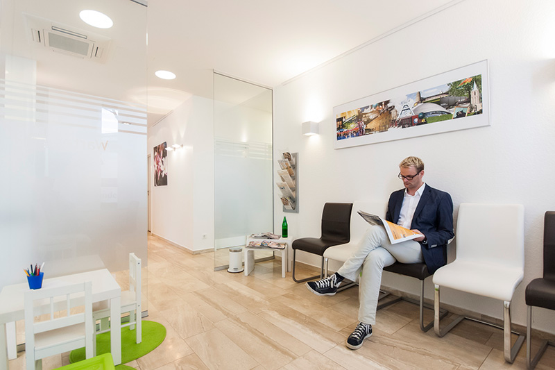 Wartezimmer der Praxis Dr. Pawlak, ein Patient liest eine Zeitschrift, daneben eine Kinderspielecke